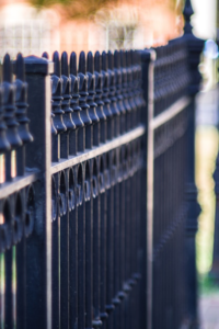 Close-up of a black metal fence with vertical bars along a concrete sidewalk.