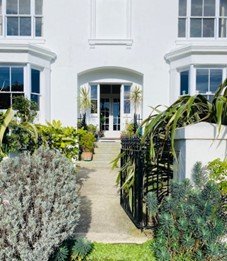 A charming white house facade surrounded by greenery, featuring a decorative wrought iron gate.